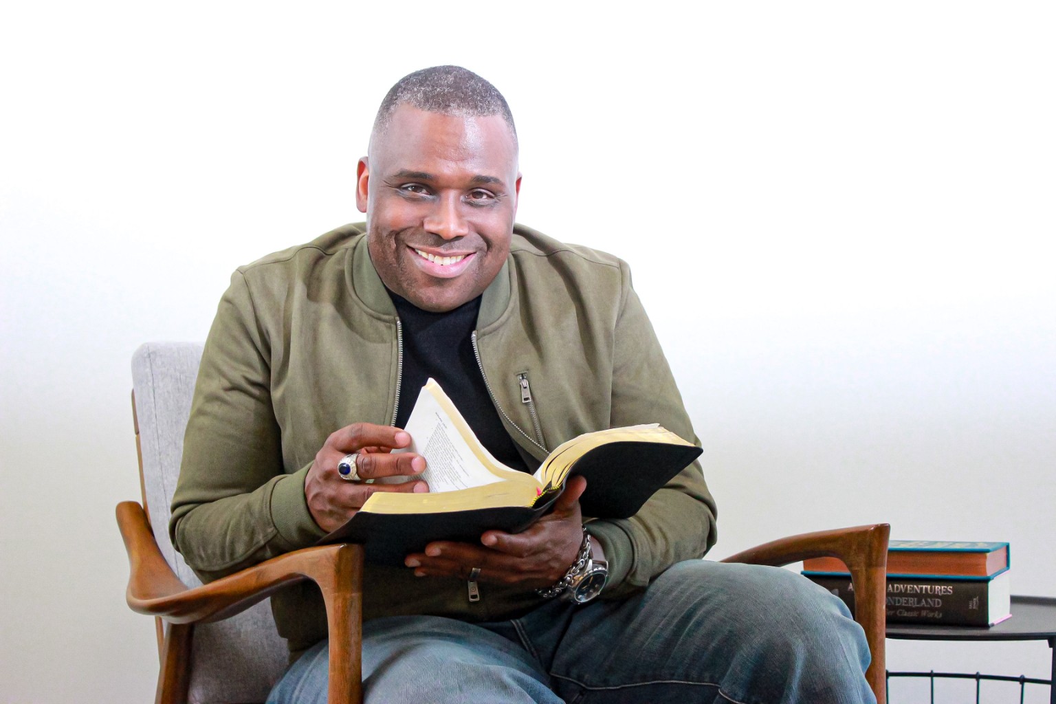 Dr. Lee P. Christian, Jr. seated in blue jeans and an olive jacket, holding an open Bible